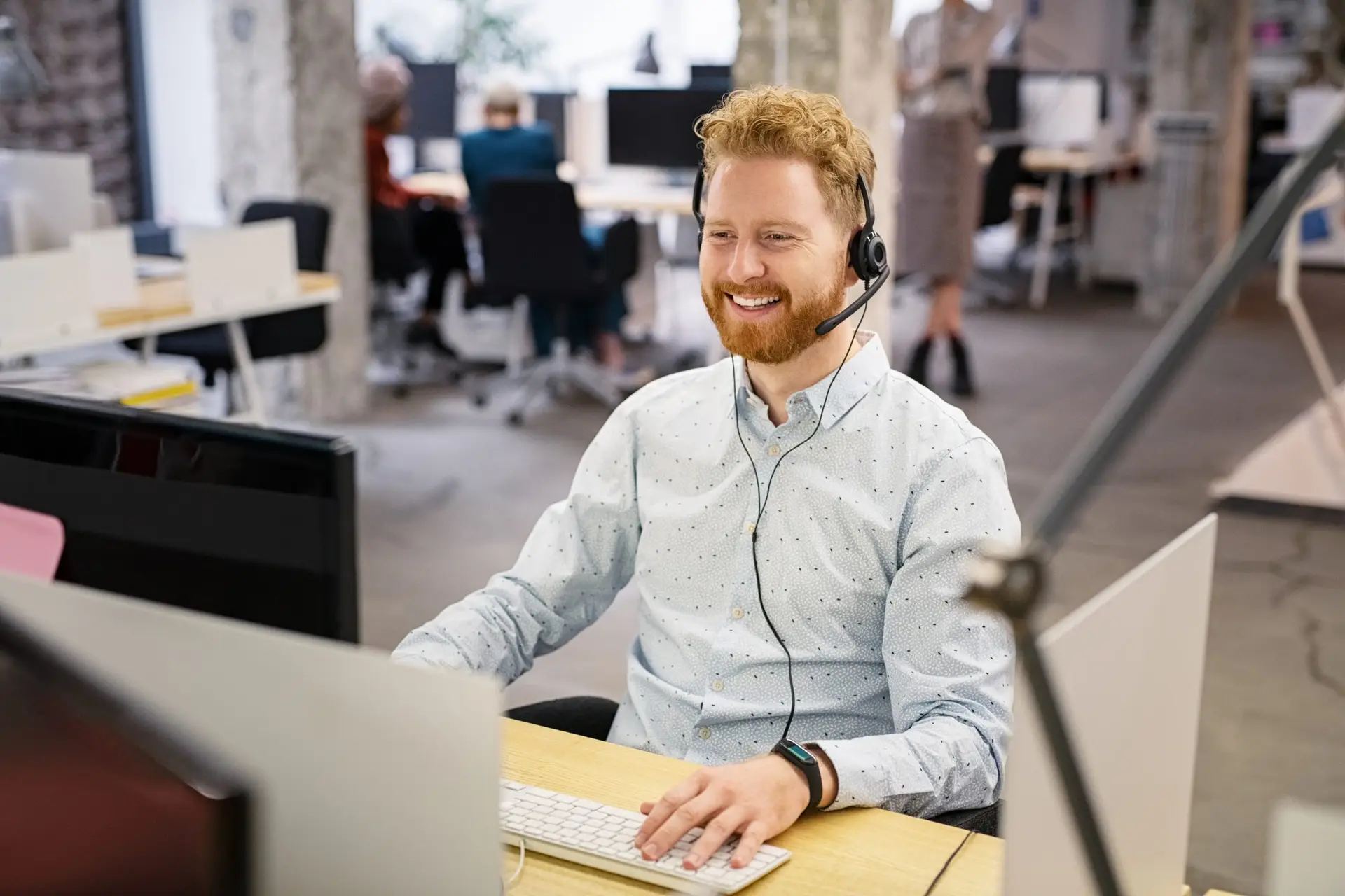 Servicedeskmedewerker met een headset die typt achter twee beeldschermen in een kantoortuin